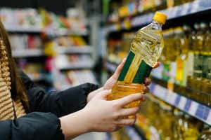 2HKYX4G Mujer eligiendo aceite de girasol en un supermercado.  Cierra la mano sosteniendo una botella de aceite en la tienda.
